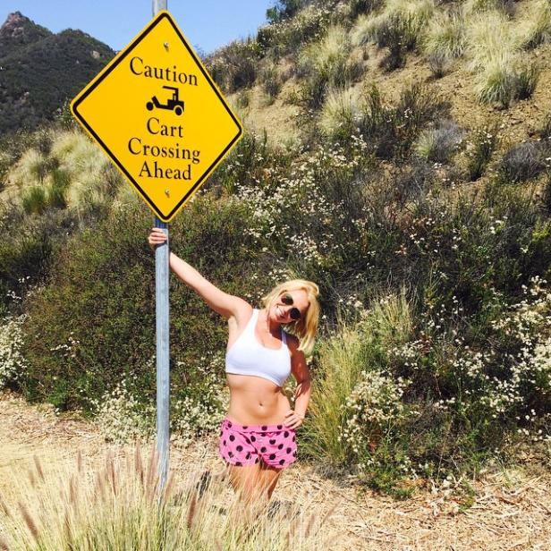 Britney Spears posiert neben einem gelben Warnschild „Achtung Golfwagen-Kreuzung“.