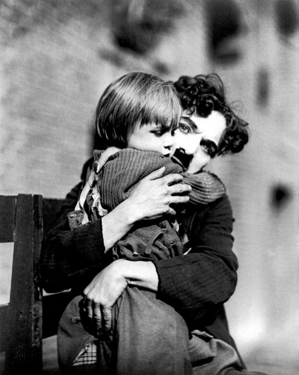 Charlie Chaplin umarmt einen kleinen Jungen in einer Szene aus dem Film „The Kid“.