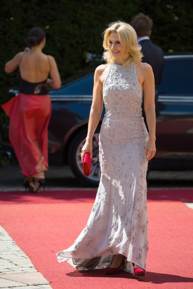 Eine blonde Frau in einem eleganten, bodenlangen Kleid auf einem roten Teppich.