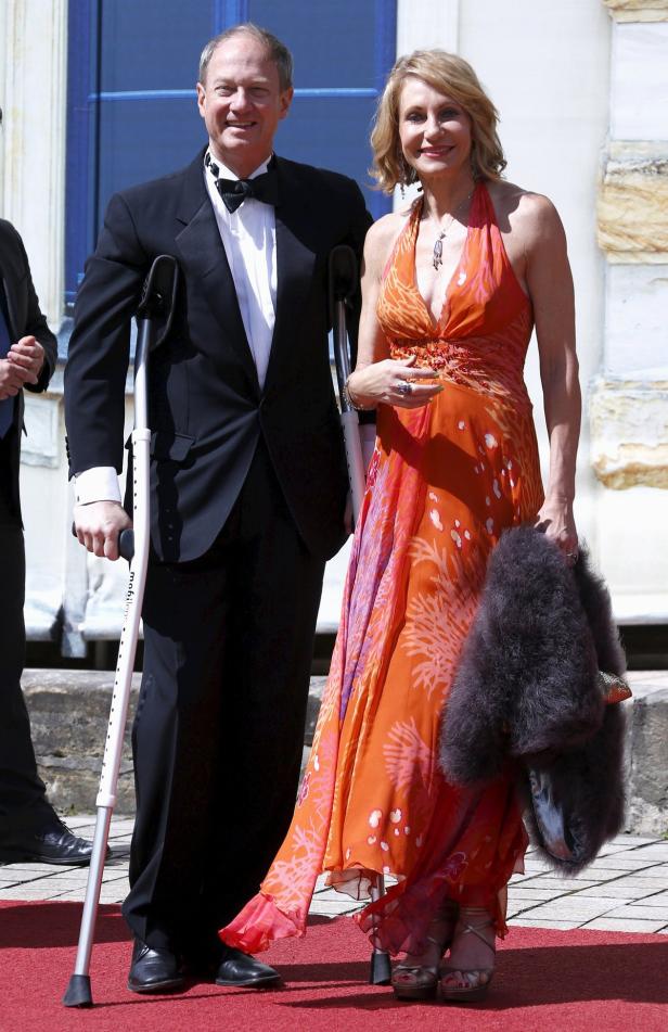 Ein Mann mit Krücken und eine Frau in einem orangefarbenen Kleid stehen auf einem roten Teppich.