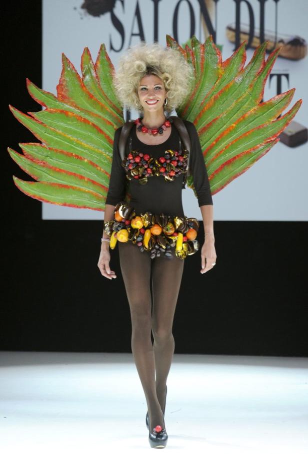Eine Frau mit Flügeln und einem Kleid aus Früchten und Süßigkeiten auf einer Modenschau.