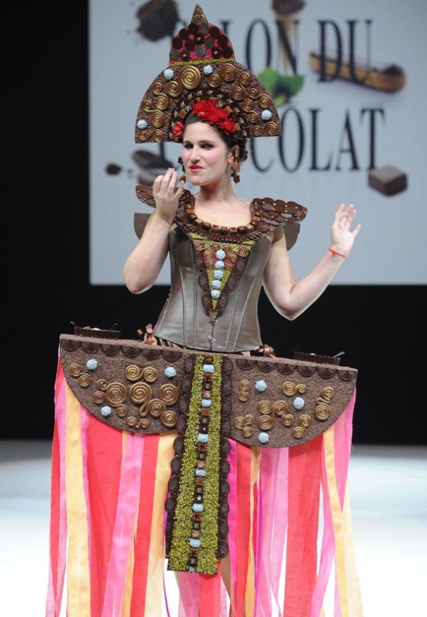 Eine Frau präsentiert ein aufwendiges Kleid aus Schokolade auf einer Bühne.