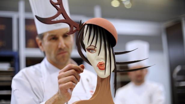 Ein Konditor dekoriert eine Schokoladenskulptur einer Frau mit Hut.