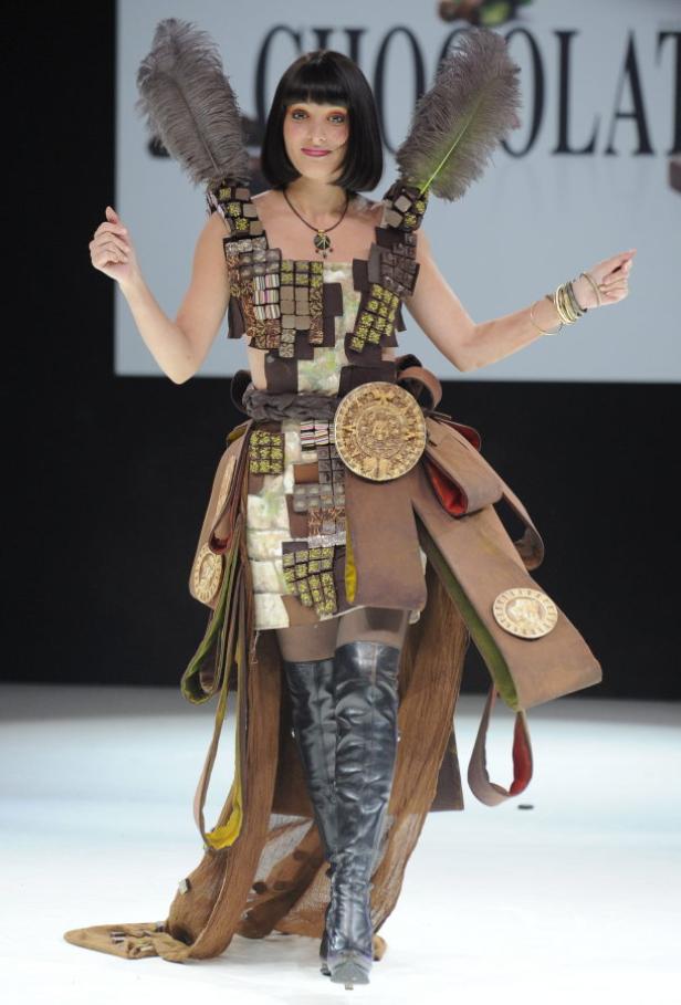 Eine Frau präsentiert ein aufwendiges Kleid aus Schokolade und Federn auf einem Laufsteg.