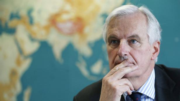 Michel Barnier vor einer Weltkarte, die Hand ans Kinn gelegt.