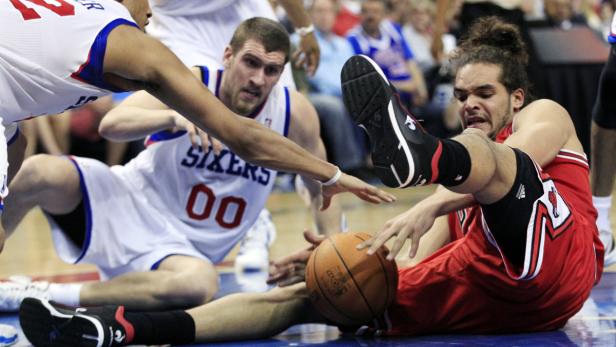 Ein Basketballspieler in Rot liegt am Boden, während andere Spieler nach dem Ball greifen.