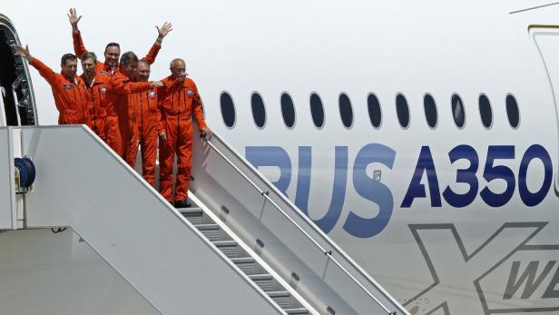 Eine Gruppe von Piloten in orangefarbenen Overalls verlässt ein Airbus A350 Flugzeug.