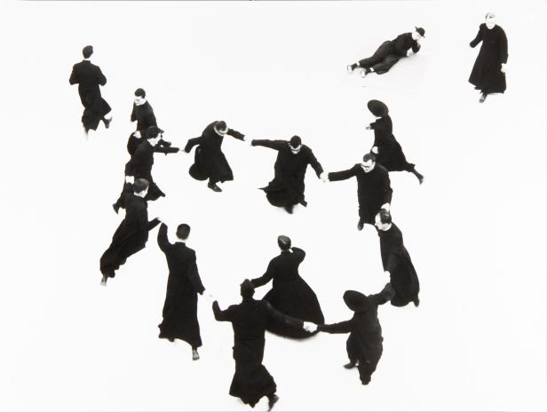 Eine Gruppe von Männern in schwarzen Gewändern tanzt im Kreis, während ein Mann daneben liegt.