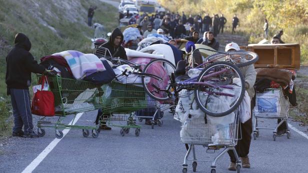 Eine Gruppe von Menschen schiebt Einkaufswagen voller Habseligkeiten eine Straße entlang.