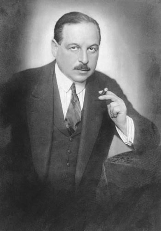 Ein Mann mit Anzug und Krawatte hält eine Zigarre in der Hand.