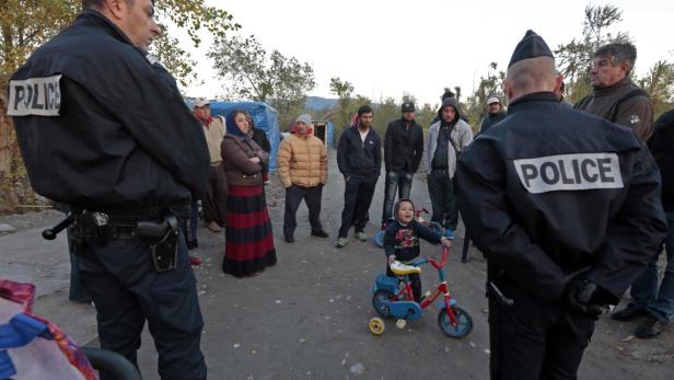 Ein kleiner Junge fährt auf einem roten Dreirad, umgeben von Polizisten und einer Gruppe von Menschen.