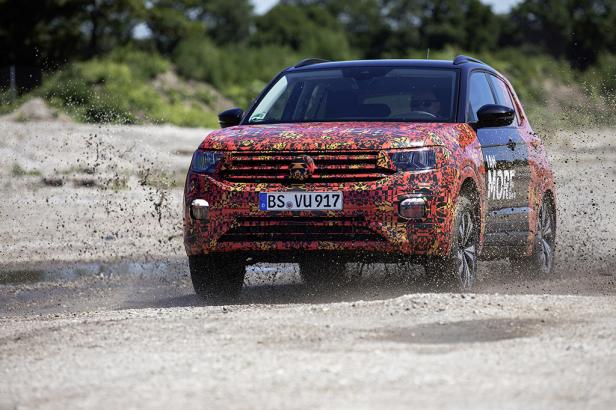 Ein rot gemusterter VW T-Cross fährt auf einer unbefestigten Straße und wirbelt Staub auf.