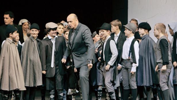 Ein Mann in einem Anzug steht vor einer Gruppe von Jungen in Kostümen auf einer Bühne.
