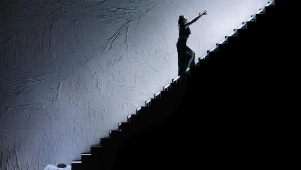 Eine Frau in einem Kleid steigt eine Treppe vor einer strukturierten Wand hinauf.