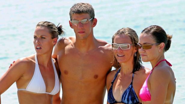 Michael Phelps posiert mit drei Frauen am Strand.