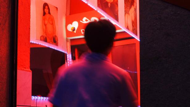 Ein Mann steht vor einem Schaufenster mit roter Beleuchtung und erotischen Bildern.