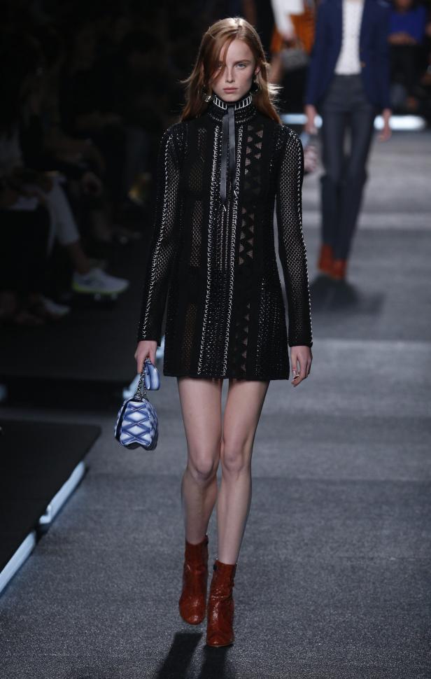 Ein Model läuft in einem schwarzen Kleid und roten Stiefeln über den Laufsteg.