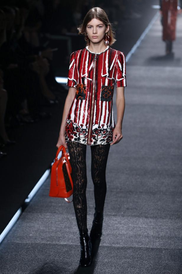 Ein Model auf dem Laufsteg mit einem rot-weiß gestreiften Kleid und einer orangefarbenen Handtasche.