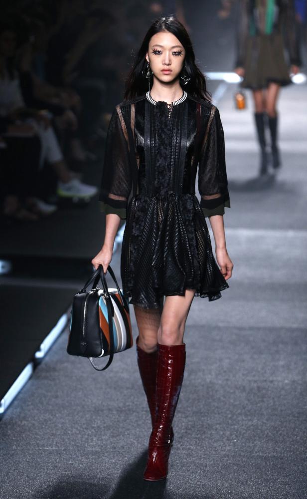 Eine Frau mit einem schwarzen Kleid und roten Stiefeln auf dem Laufsteg.