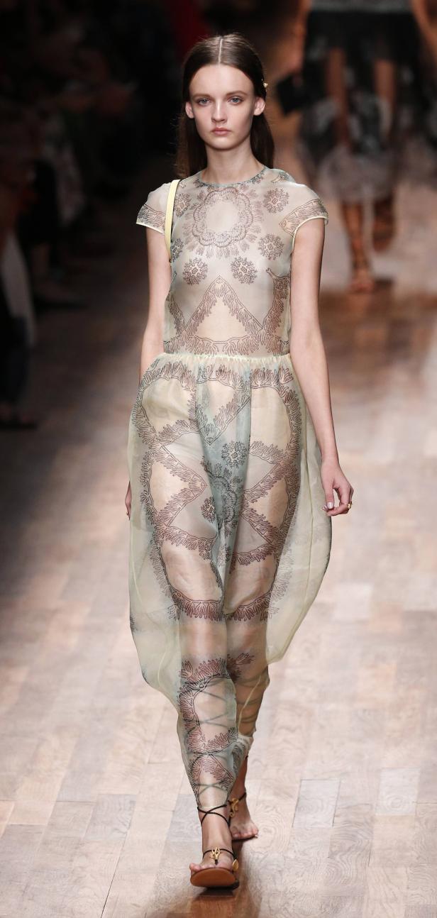 Ein Model präsentiert ein transparentes Kleid mit floralen Mustern auf dem Laufsteg.