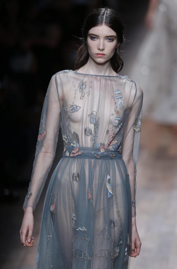 Ein Model präsentiert ein transparentes, blaues Kleid mit Meeresmotiven auf dem Laufsteg.