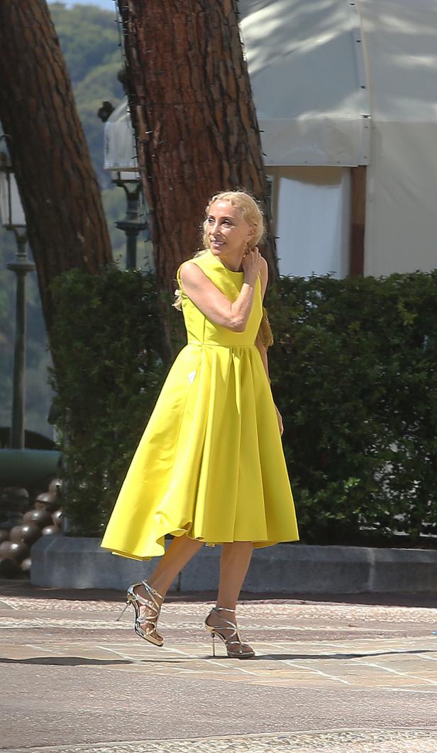 Eine Frau in einem gelben Kleid und silbernen High Heels geht auf einem Platz.