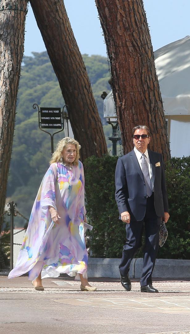 Eine ältere Frau in einem bunten Kleid und ein Mann im Anzug gehen zusammen spazieren.