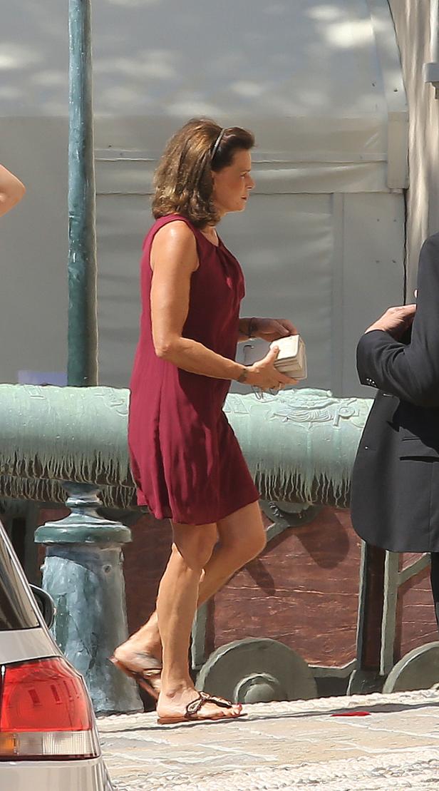 Eine Frau in einem roten Kleid und Sandalen trägt eine kleine, rechteckige Tasche.