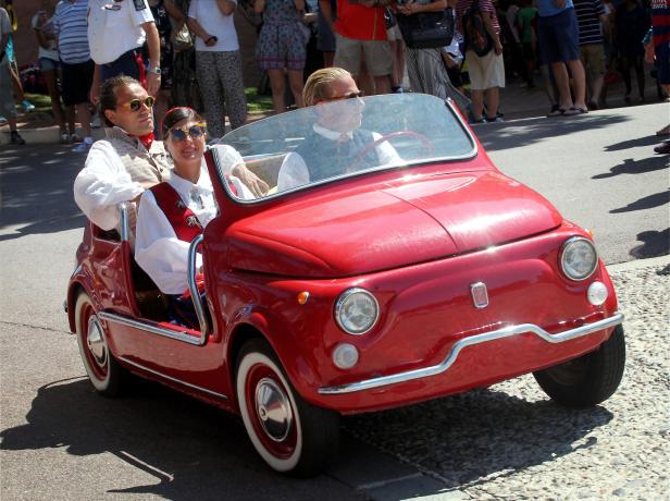 Drei Personen fahren in einem roten Oldtimer-Cabriolet.