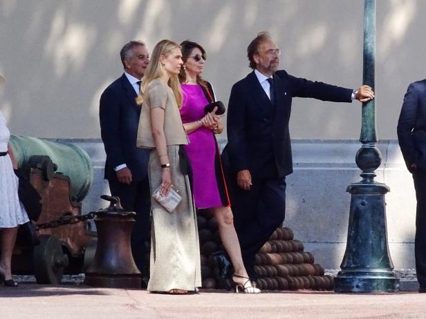 Eine Gruppe elegant gekleideter Menschen steht im Freien neben einer Kanone.