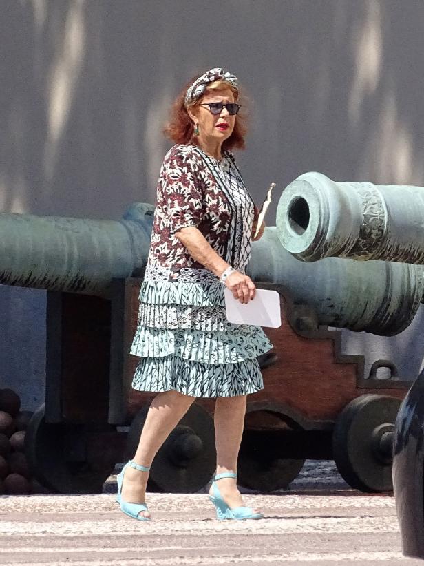 Eine Frau mit Sonnenbrille geht an alten Kanonen vorbei.