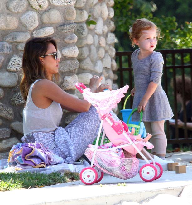 Jessica Alba sitzt mit ihrer Tochter und einem Puppenwagen im Freien.