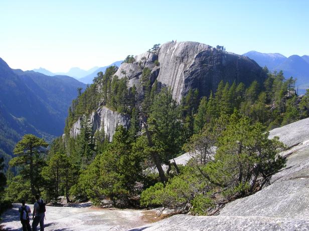 Blick auf einen felsigen Berggipfel mit Bäumen und Wanderern im Squamish, British Columbia.