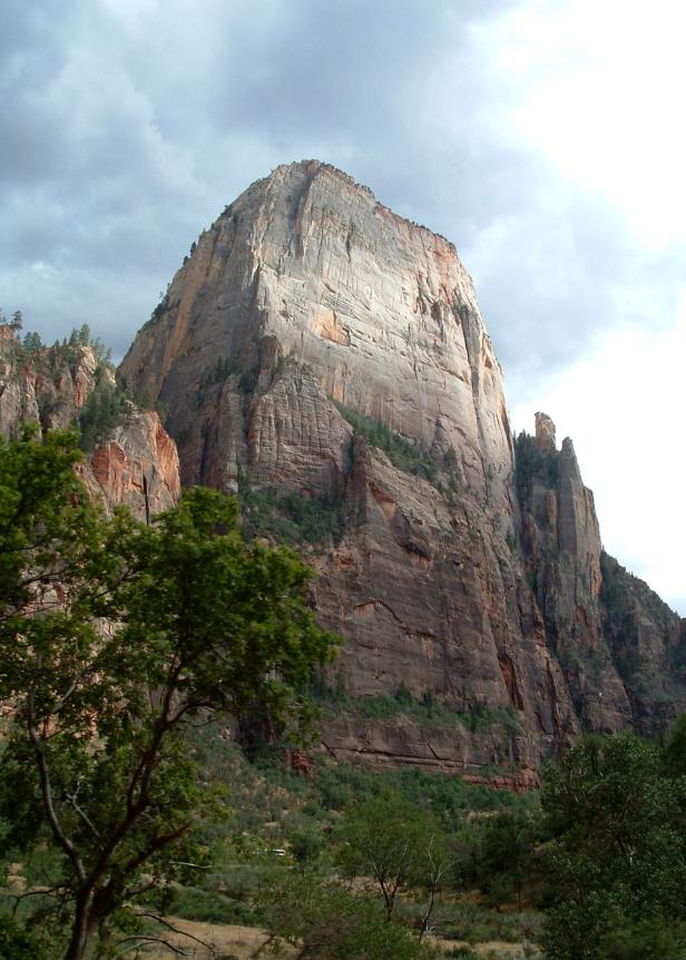 Ein großer, grauer Felsen ragt in einer bewaldeten Landschaft in den Himmel.