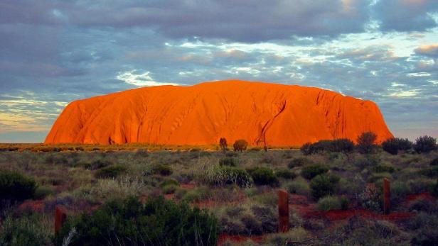 Der orangefarbene Monolith Uluru ragt aus der australischen Wüste auf.