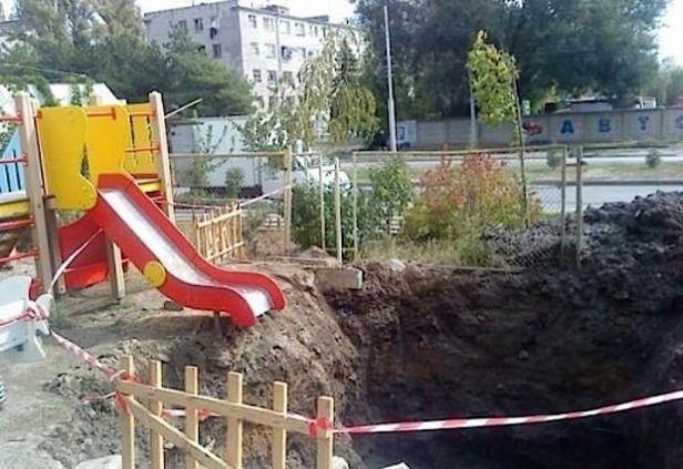 Ein Spielplatz mit einer Rutsche ist von einem tiefen Loch im Boden umgeben.