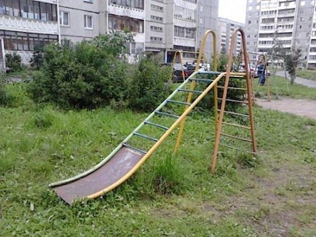 Eine alte, gelb-grüne Rutsche steht auf einer Wiese vor einem Wohnhaus.