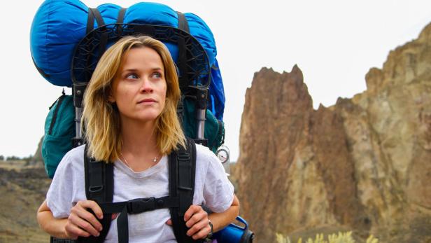 Reese Witherspoon mit großem Rucksack in einer felsigen Landschaft.