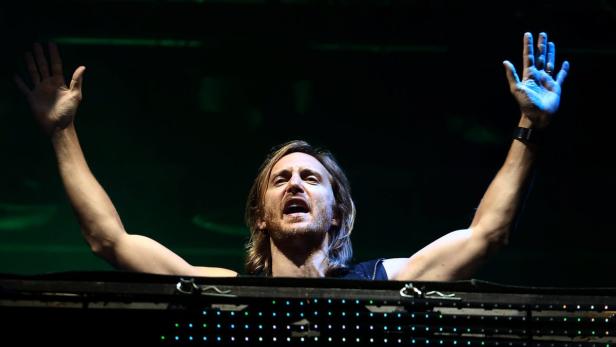 David Guetta legt bei einem Konzert auf und reißt die Arme hoch.