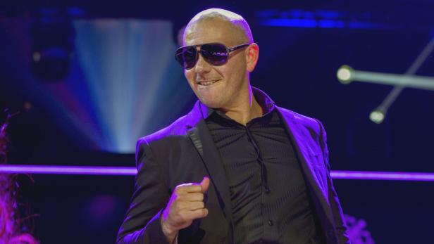 Pitbull tritt in einem schwarzen Anzug und mit Sonnenbrille auf einer Bühne auf.