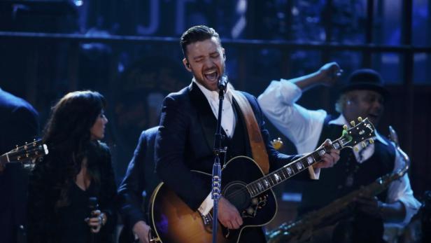 Justin Timberlake tritt mit einer Akustikgitarre auf einer Bühne auf.