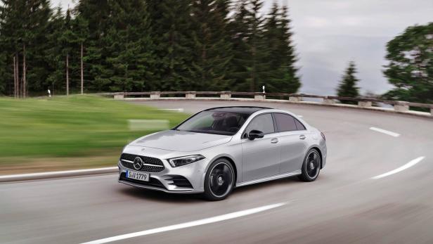Eine silberne Mercedes-Benz A-Klasse Limousine fährt auf einer kurvenreichen Straße entlang eines Waldes.