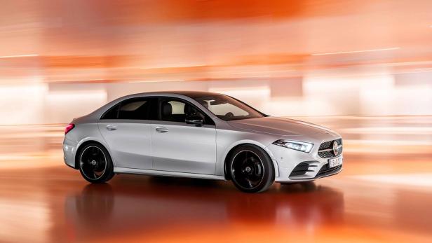 Eine silberne Mercedes-Benz A-Klasse Limousine vor einem orangefarbenen Hintergrund.