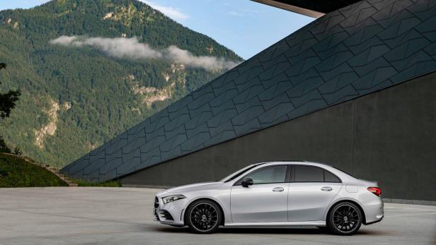 Eine silberne Mercedes-Benz A-Klasse Limousine vor einer modernen Architektur und Bergkulisse.
