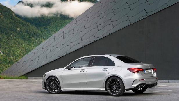Eine silberne Mercedes-Benz A-Klasse Limousine vor einer modernen Fassade und Berglandschaft.