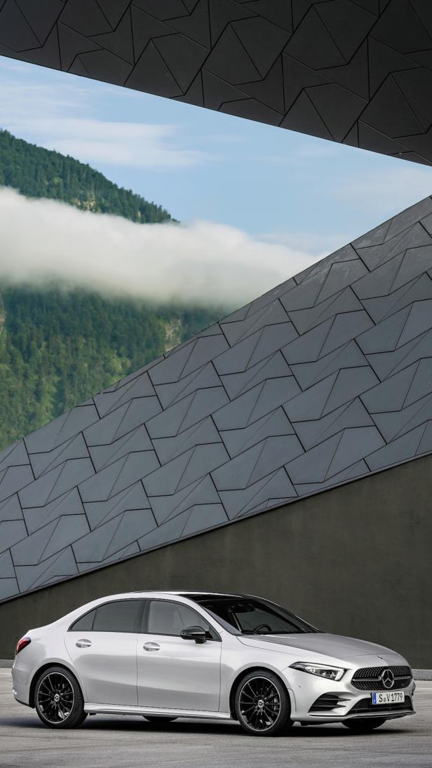 Eine silberne Mercedes-Benz A-Klasse Limousine vor einer modernen Architektur mit Bergkulisse.