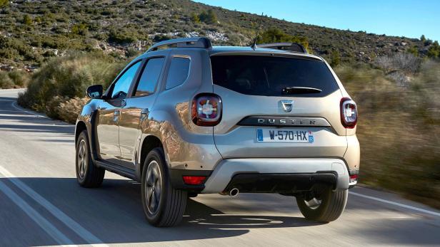 Ein goldfarbener Dacia Duster fährt auf einer kurvenreichen Straße in hügeligem Gelände.