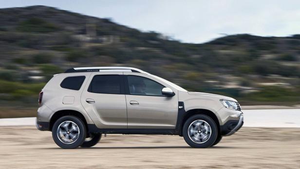 Ein beiger Dacia Duster fährt auf einer Schotterstraße.