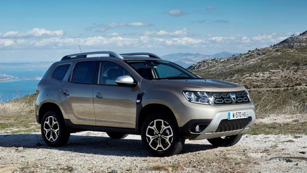 Ein goldfarbener Dacia Duster steht in einer hügeligen Landschaft.