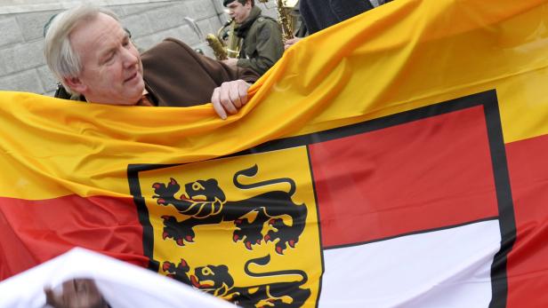 Ein Mann hält die Flagge Baden-Württembergs hoch, während im Hintergrund eine Blaskapelle spielt.